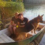 Dwie osoby i pies cieszą się spokojną przejażdżką łodzią po spokojnym jeziorze.